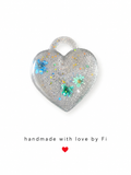 Holographic glitter resin heart pendant with iridescent sequins and blue and teal dried flowers handmade by Fi